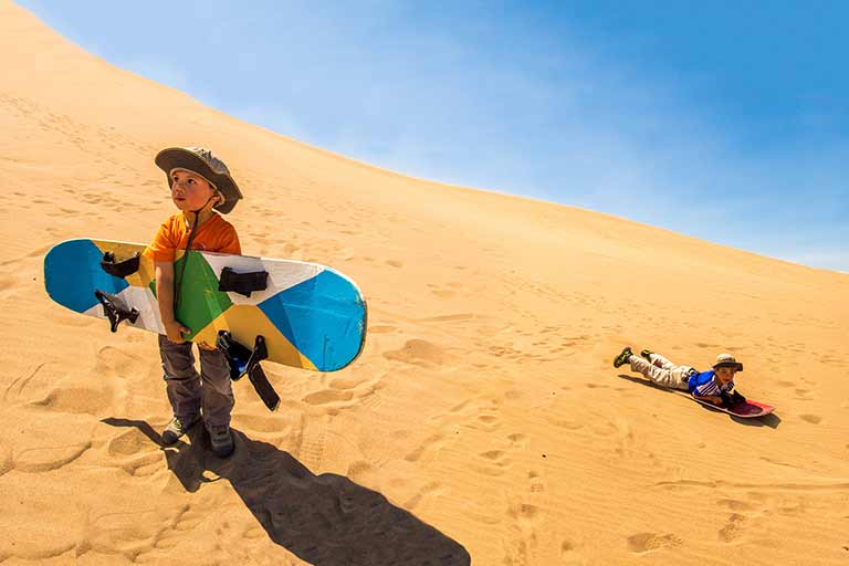 Children sandboarding in Huacachina Peru